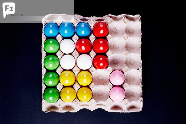 Draufsicht auf mehrfarbig bemalte Eier im Tablett auf schwarzem Hintergrund