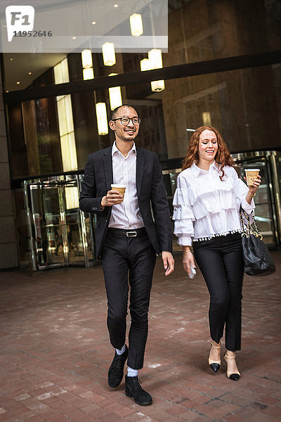 Junge Geschäftsfrau und Mann mit Kaffee zum Mitnehmen schlendern auf dem Bürgersteig  New York  USA
