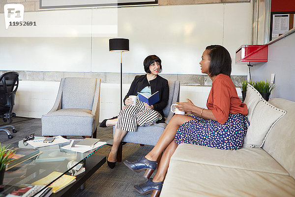 Zwei Geschäftsfrauen sitzen auf bequemen Stühlen im Büro und machen eine Kaffeepause