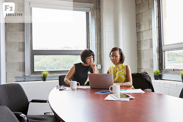 Zwei Frauen sitzen am Tisch im Sitzungssaal und benutzen einen Laptop