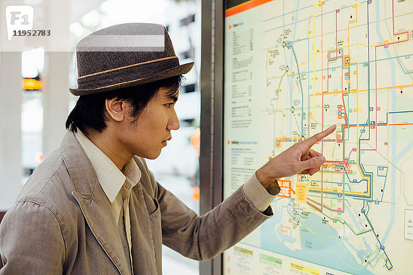 Junger Mann schaut am Bahnhof auf die Zugkarte