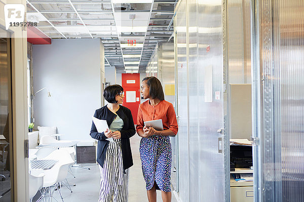 Zwei Geschäftsfrauen gehen den Bürokorridor entlang  im Gespräch