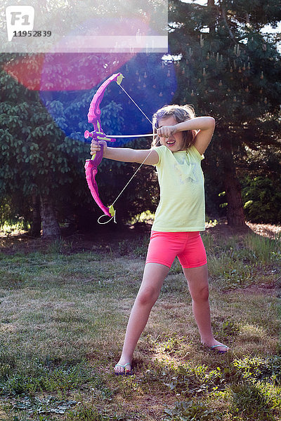 Junges Mädchen spielt mit Pfeil und Bogen im Garten