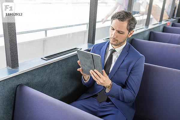 Junger Geschäftsmann auf Passagierfähre sieht sich digitales Tablet an