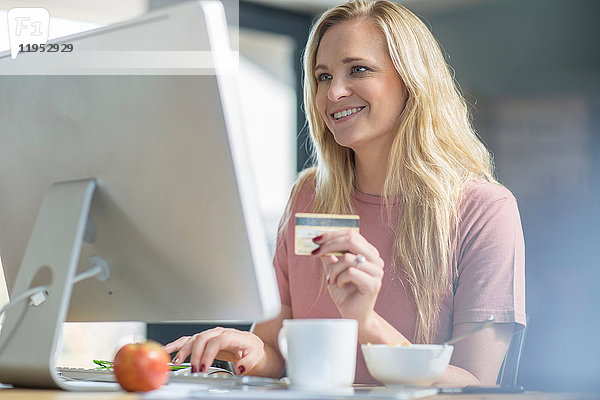 Frau hält Kreditkarte und benutzt Computer lächelnd