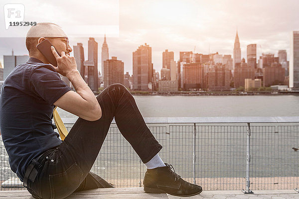 Geschäftsmann sitzt am Wasser und telefoniert mit seinem Smartphone  New York  USA