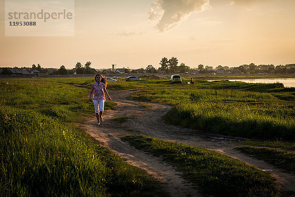 Einsames Teenagermädchen rennt bei Sonnenuntergang auf ländlichem Feldweg