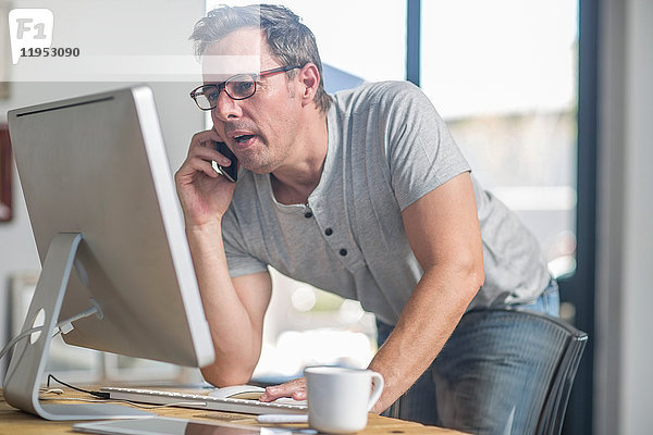 Mann am Computer mit Smartphone zum Telefonieren