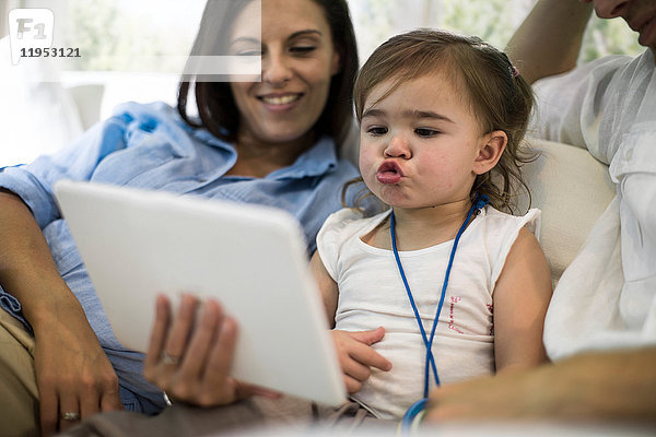 Ehemann und Ehefrau benutzen digitales Tablet mit Mädchen auf dem Sofa