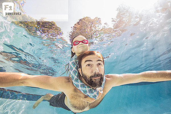 Unterwasseransicht eines reifen Mannes  der mit der Tochter auf dem Huckepack schwimmt