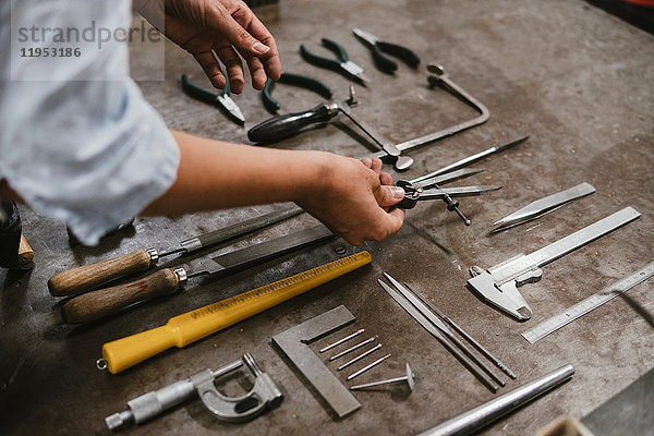 Hände einer Juwelierin beim Auslegen von Handwerkzeugen an der Werkbank in der Schmuckwerkstatt