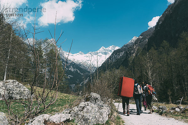 Rückansicht von erwachsenen Freunden mit Bouldermatten-Rucksack beim Wandern entlang einer Landstraße  Lombardei  Italien
