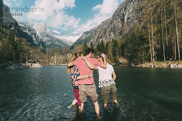 Rückansicht von drei jungen erwachsenen Freunden knöcheltief im Bergsee  Lombardei  Italien