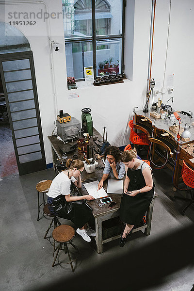 Hochwinkelansicht von drei Juwelierinnen  die bei einem Arbeitstreffen auf den Skizzenblock schauen
