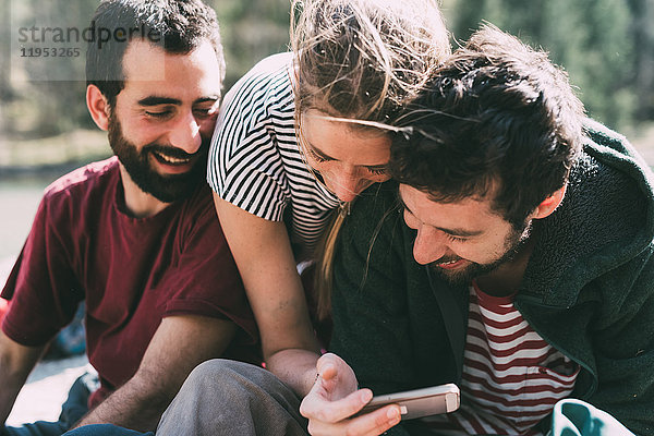 Drei junge erwachsene Freunde schauen und lachen über Smartphone  Lombardei  Italien