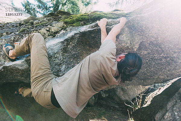 Junge männliche Boulderer klettern an der Kante eines Felsblocks  Lombardei  Italien