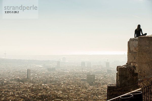 Von hinten beleuchtete weibliche Touristin  die von der Spitze einer Mauer auf das Stadtbild von Barcelona blickt  Spanien