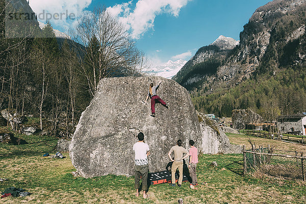 Rückansicht von erwachsenen Boulderfreunden  die einer jungen Frau beim Bouldern zuschauen  Lombardei  Italien