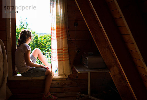 Teenager-Mädchen sitzt auf der Fensterbank im Schlafzimmer und schaut auf das Sonnenlicht