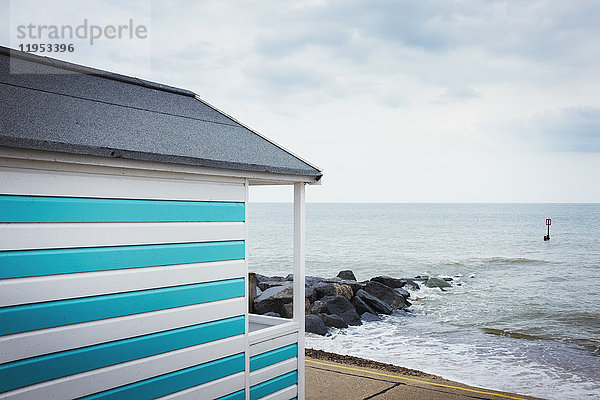 Eine blau-weiß gestreifte Strandhütte an einem Strand an der Küste.