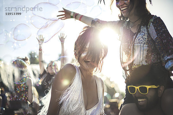 Schwelgender junger Mann mit gelber Sonnenbrille und Frau auf den Schultern bei einem Sommer-Musikfestival.