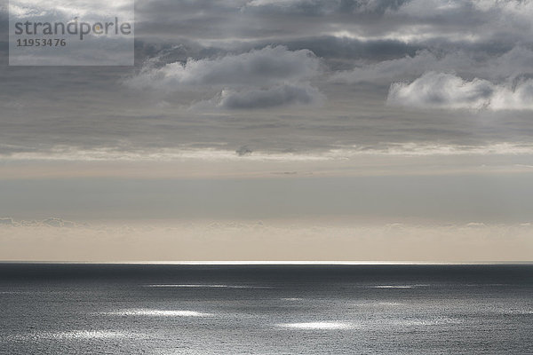 Blick vom Land über den Ozean  bei schwachem Licht bis zum Horizont. Sonnenlichtflecken auf der Wasseroberfläche. Rosa und blauer Himmel in der Dämmerung