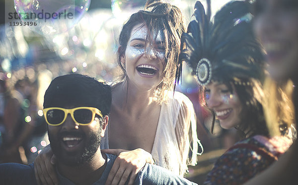 Schwelgt bei einem Sommer-Musikfestival junger bärtiger Mann mit gelber Sonnenbrille und Frauen mit Federkopfschmuck und bemalten Gesichtern.