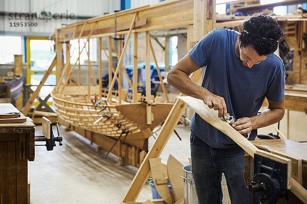 Mann  der in der Werkstatt eines Bootsbauers steht und an einem hölzernen Ruder arbeitet.