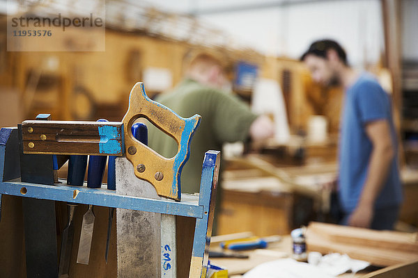 Nahaufnahme der Handwerkzeuge in der Bootsbauwerkstatt  zwei Männer arbeiten im Hintergrund.