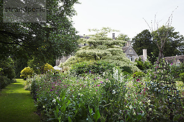 Außenansicht eines Landhauses aus dem 17. Jahrhundert von einem Garten mit Blumenbeeten  Sträuchern und Bäumen aus.