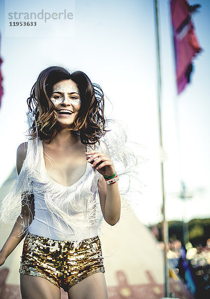 Junge Frau bei einem Sommer-Musikfestival in goldenen  mit Pailletten bestickten Hotpants  geschminktes Gesicht  lächelt in die Kamera.