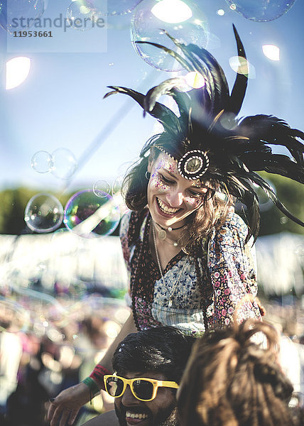 Nachtschwärmer bei einem Sommer-Musikfestival junger Mann mit gelber Sonnenbrille  der eine Frau mit Federkopfschmuck auf den Schultern trägt.