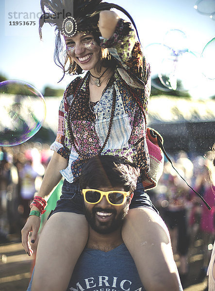 Nachtschwärmer bei einem Sommer-Musikfestival junger Mann mit gelber Sonnenbrille  der eine Frau mit Federkopfschmuck auf den Schultern trägt.