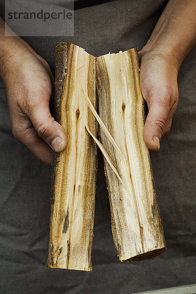 Nahaufnahme einer Person  die zwei Stücke eines in zwei Hälften gespaltenen Holzstammes hält. Äste und Muster der Holzmaserung.