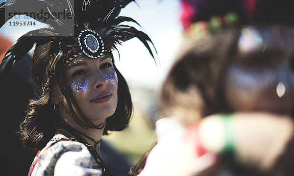 Junge Frau bei einem Sommer-Musikfestival mit geschminktem Gesicht  Federkopfschmuck und Blick in die Kamera.