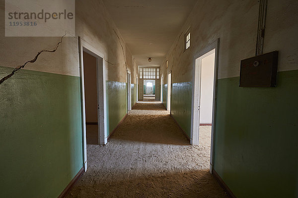 Blick auf einen Korridor in einem heruntergekommenen Gebäude voller Sand. Lebhaft grün gefärbte Wände. Schatten
