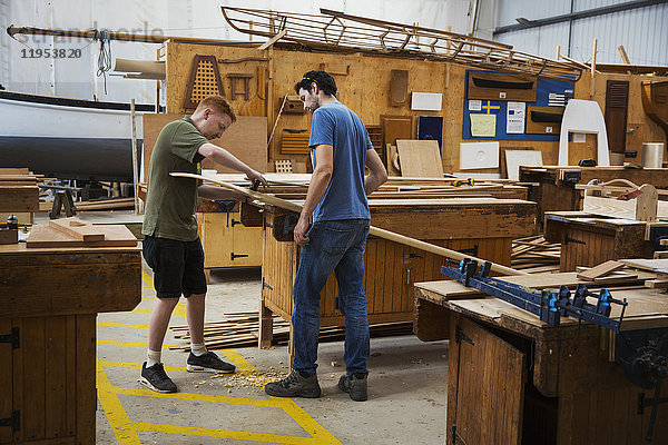 Zwei Männer stehen an einer Werkbank in der Werkstatt eines Bootsbauers und arbeiten an einem Stück Holz.