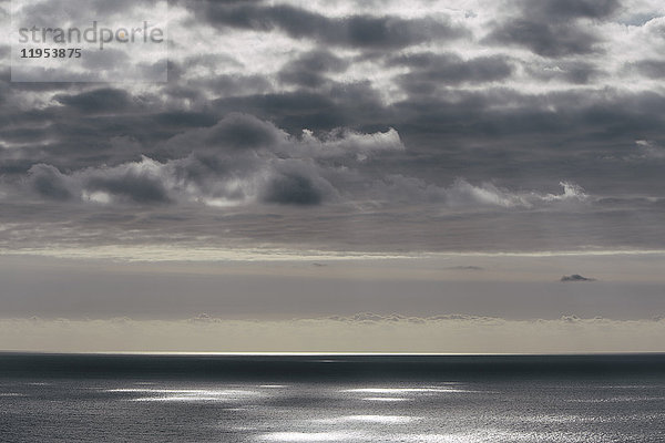Blick vom Land über den Ozean  bei schwachem Licht bis zum Horizont. Sonnenlichtflecken auf der Wasseroberfläche.