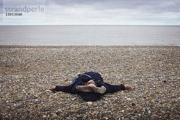 Auf dem Rücken liegende Frau an einem Kieselstrand am Meer.
