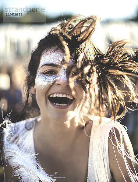 Junge Frau mit langen braunen Haaren bei einem Sommer-Musikfestival mit geschminktem Gesicht  in die Kamera lächelnd.