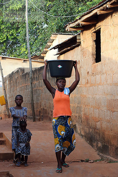 Afrikanisches Dorfleben. Wasserarbeit. Afrikanisches Mädchen trägt eine Schüssel mit Wasser auf dem Kopf. Togoville. Togo.