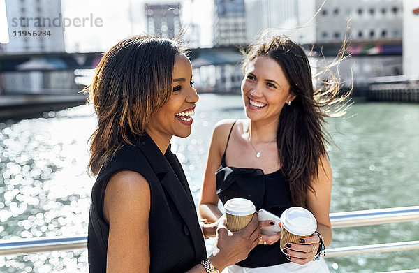 Zwei glückliche Frauen bei einer Kaffeepause auf einer Brücke in der Stadt
