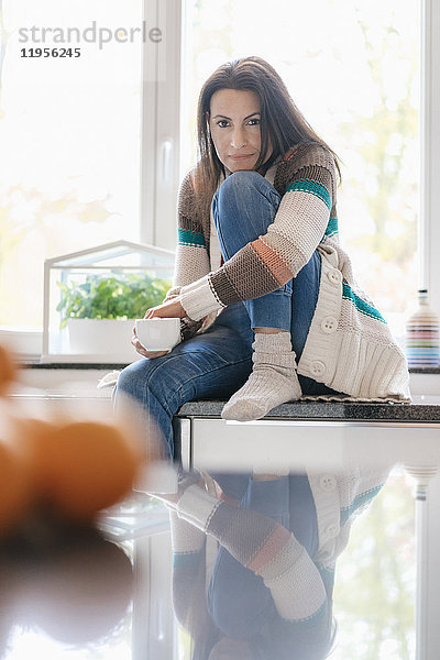 Porträt einer Frau zu Hause  die auf der Küchenzeile sitzt.