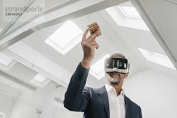 Älterer Geschäftsmann im Büro mit VR-Brille mit Rubik's Cube