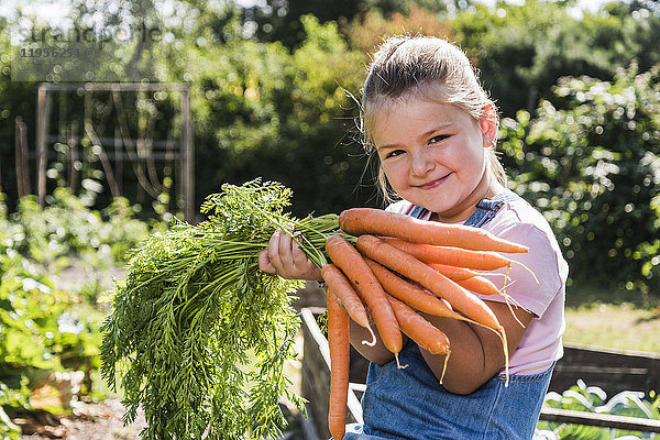 Porträt des lächelnden Mädchens im Garten mit Karottenstrauß