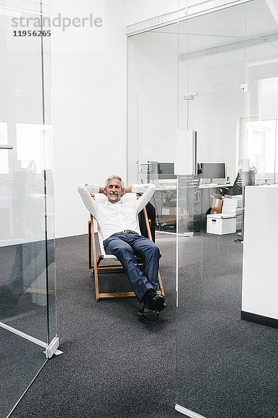 Lächelnder reifer Geschäftsmann entspannt auf dem Liegestuhl im Büro