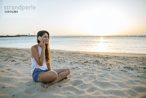 Junge Frau beim Telefonieren am Strand bei Sonnenuntergang