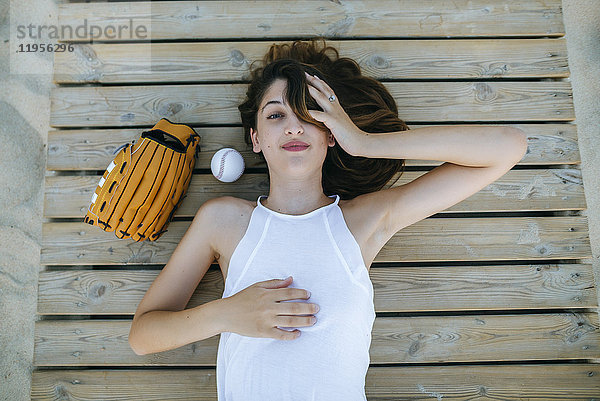 Junge Frau auf Holzweg neben Ball und Baseballhandschuh liegend