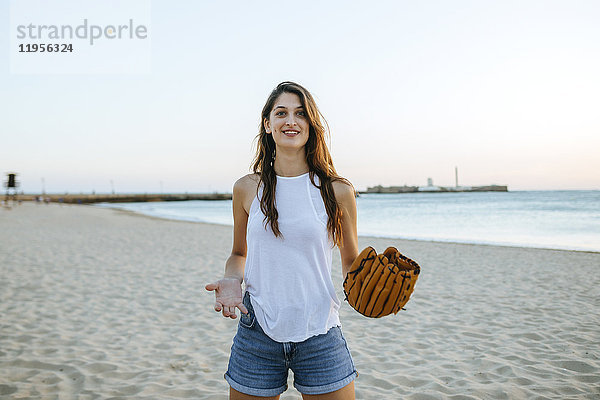 Junge Frau beim Spielen mit Baseballhandschuhen am Strand bei Sonnenuntergang