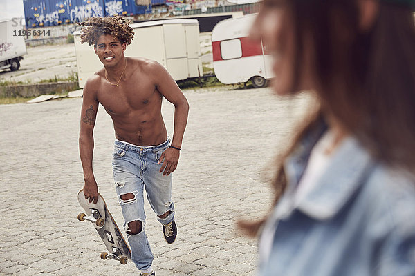 Junger Mann mit Skateboard  der zu seiner Freundin rennt.